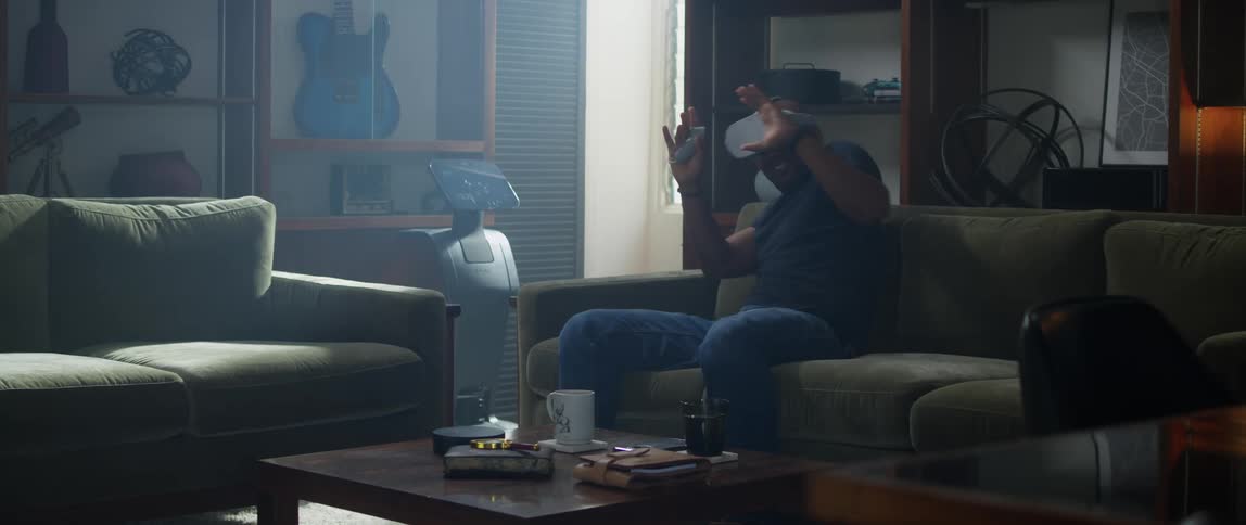 Man wearing black t shirt and jeans sits on green couch uses virtual reality in the living room