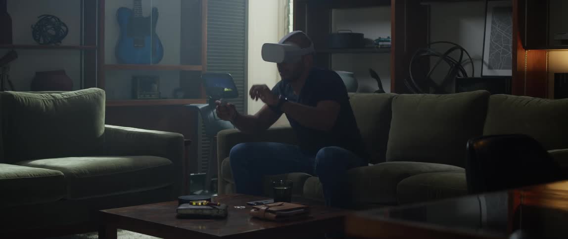 A man is sitting on the couch wearing a virtual reality headset while swinging his arms while playing a game