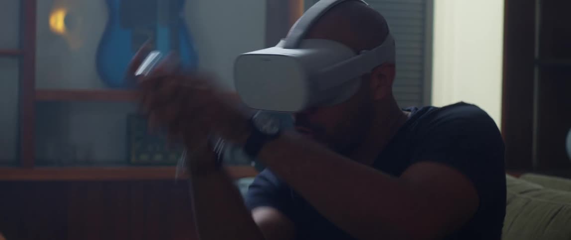 A man is sitting on the couch wearing a virtual reality headset while moving his arms round while playing a game