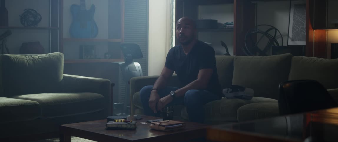 A man sits on a couch at home and takes off virtual reality goggles and takes a drink of water