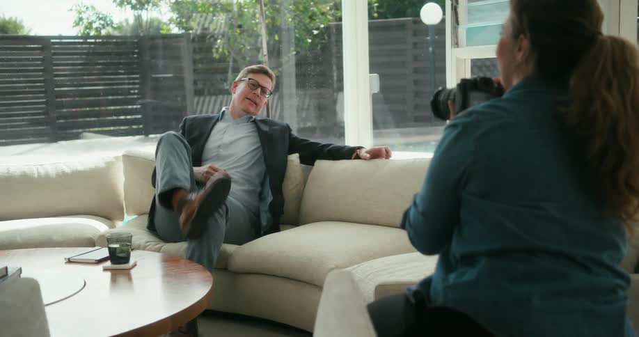Photographer takes pictures of a business man sitting on a couch at home