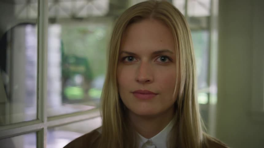 A woman with blonde hair turns and looks directly at the camera