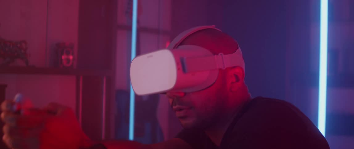 Man wearing virtual reality headset and black t-shirt plays game in dark room