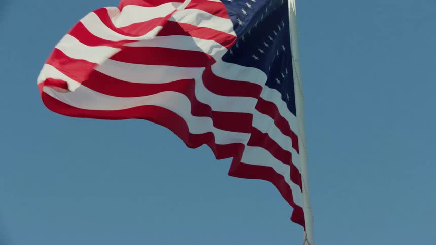 The sun shines upon an american flag as it waves in the wind in a clear sky