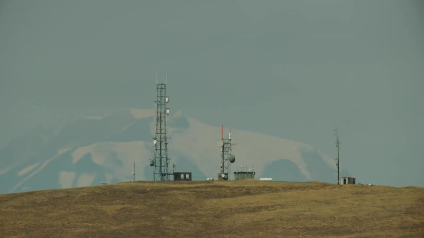 A snow covered mountain stands next to a hilltop with several cell phone towers and antennas showing the infrastructure that keeps America running