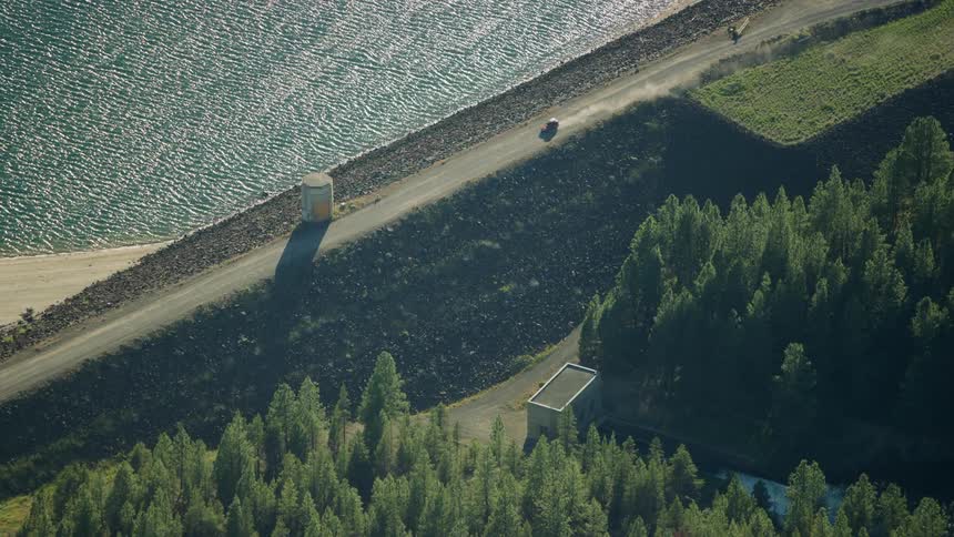 A vehicle drives along a dirt road dam road above a drying out reservoir in the Western USA