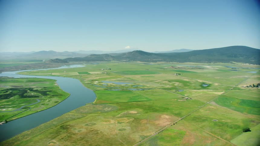An aerial view of a river running through a grassland with hills in the distance near Klamath Falls, Oregon