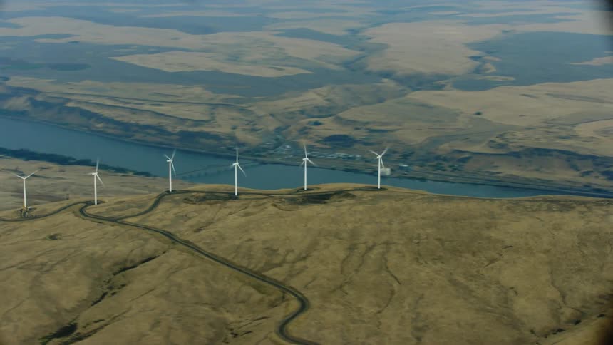 Hyper lapse aerial view of wind turbines on a wind farm atop a mountain near a river communicating rapidly generated clean and renewable energy