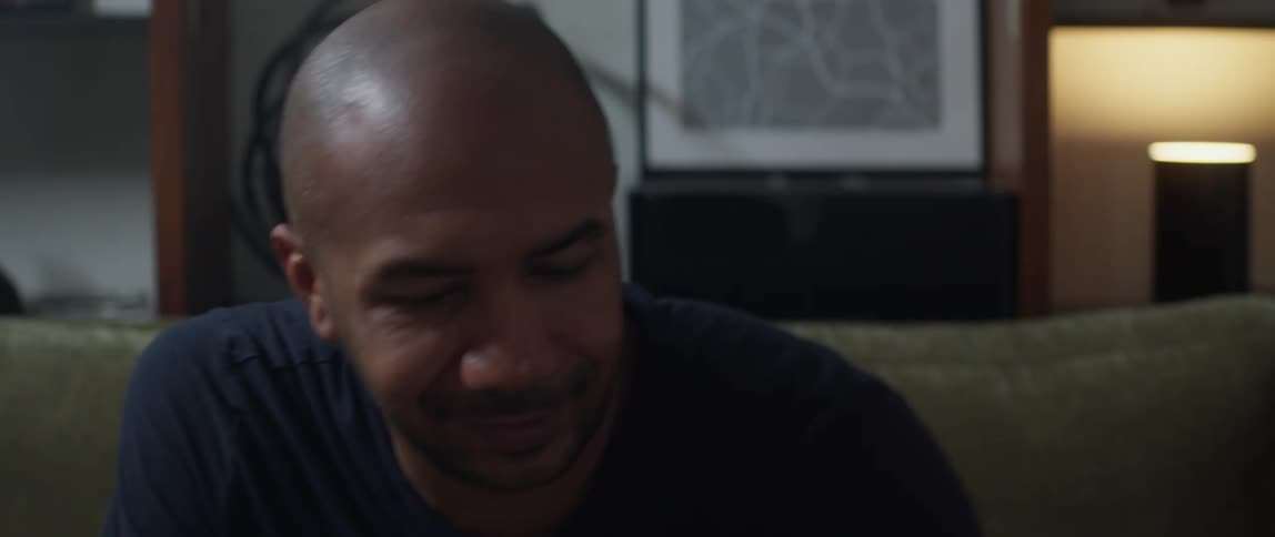 Man sitting down on couch while looking at his phone smiling like hes happy to see whats on it