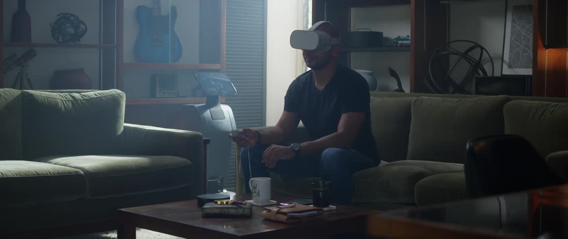 A man calmly sits on the couch while wearing a virtual reality headset