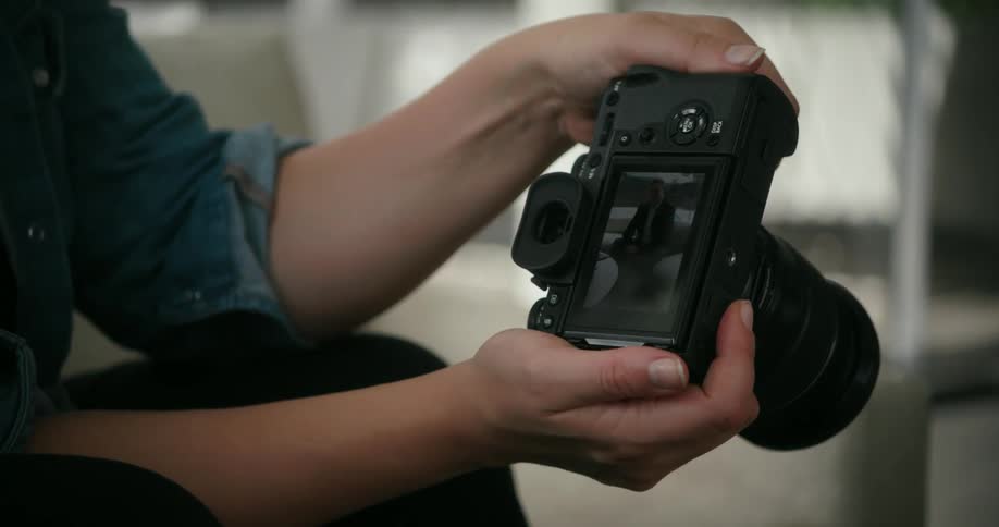 A woman holds a camera and looks at photos of a man posing
