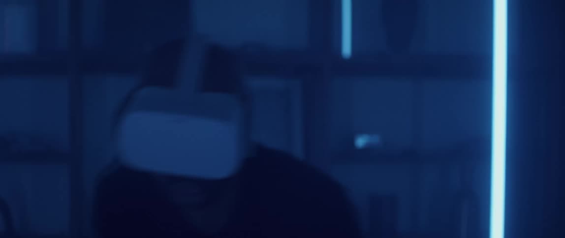 A man is standing in a room wearing a virtual reality headset and moving his arms with a remote controller as he gets into the action and lights flash in the room