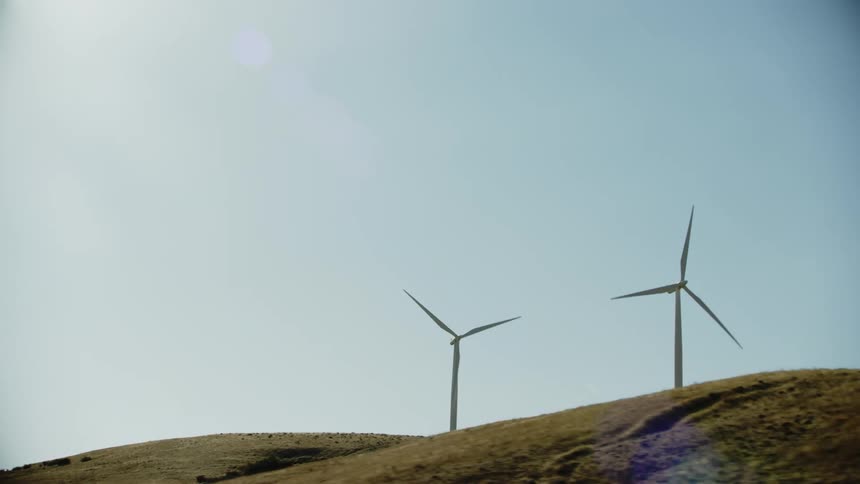 Two wind turbines whirling atop a mountain from this low altitude aerial under the hot desert sun in summer