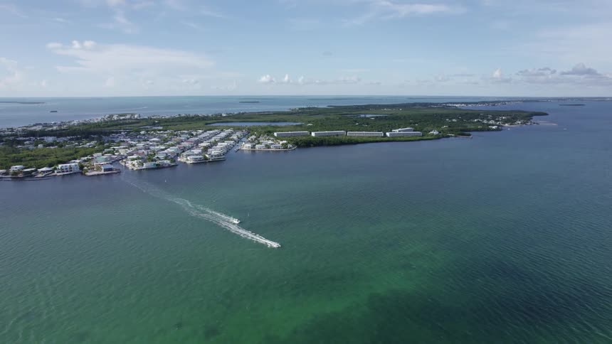 Two motor boats speed away from marina on heavily forested island