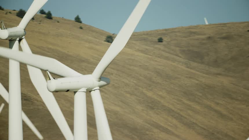 Low altitude aerial tight shot zoomed in on several wind mills generating clean energy on a wind farm