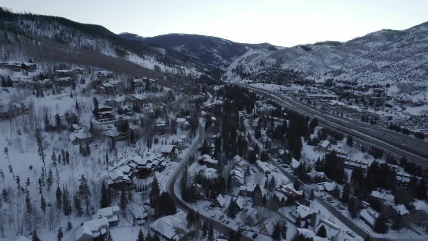 Vehicles drive down a highway through a snow covered mountain town