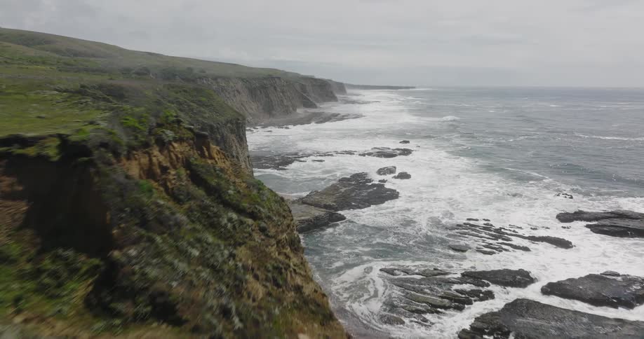 Waves crash against beach and seaside cliffs on foggy overcast day