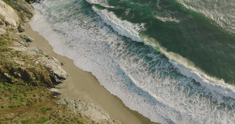 Aerial view of the gentle ocean waves crashing on the sand beach in the coast