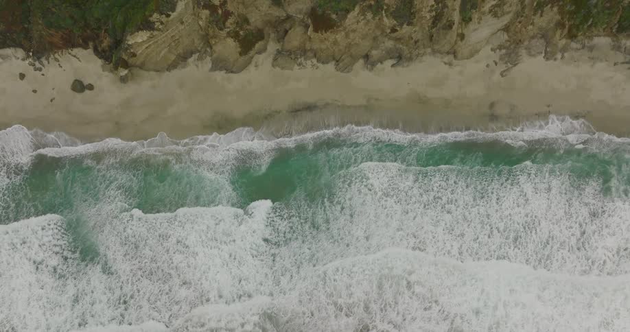 Top down aerial view of waves gently crashing on the sand beach in the coast