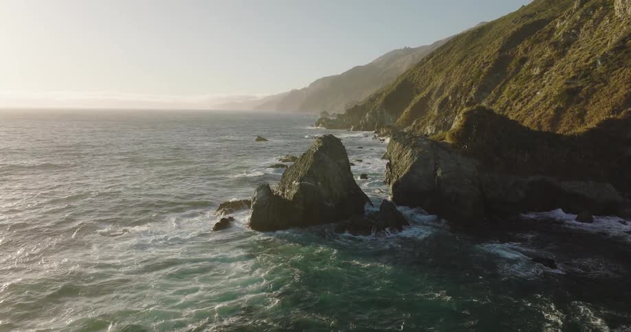 Aerial top down view of the rugged coast where mountains meet the ocean at evening