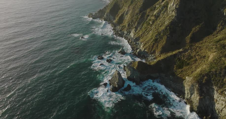 Aerial top down view of the rugged coast where mountains meet the ocean at evening