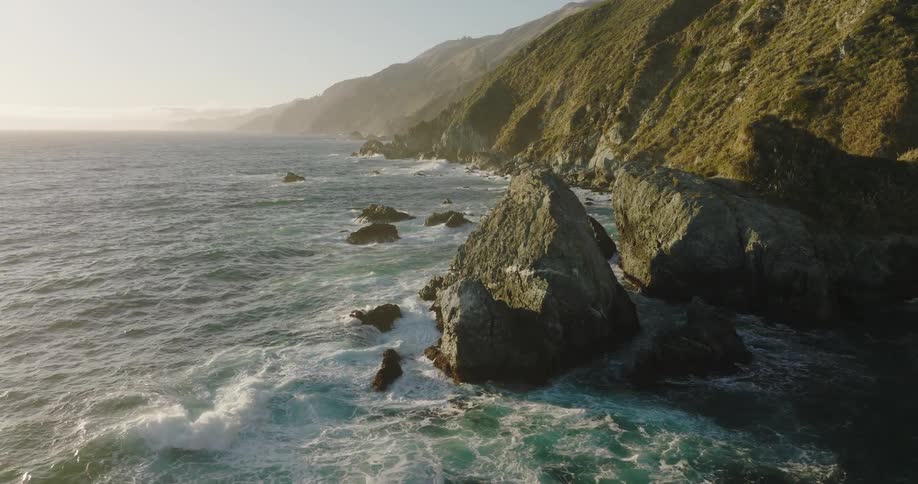 Aerial view of promontories on the rugged coast where mountains meet the ocean at evening