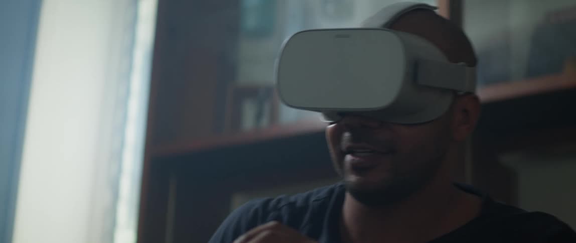 A man wearing a virtual reality headset looks around swings his controller wildly during his game