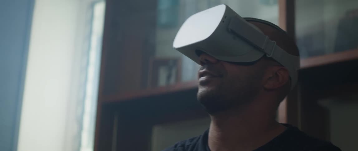 Man wearing black t shirt and virtual reality headset plays video game in the living room