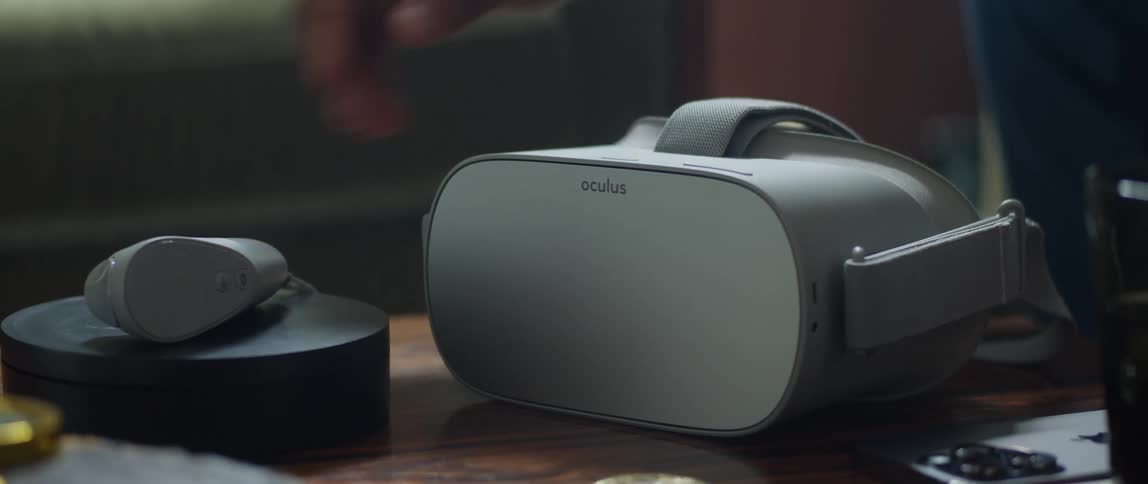 An oculus virtual reality headset and controller are on a table and a man standing near the table picks them up
