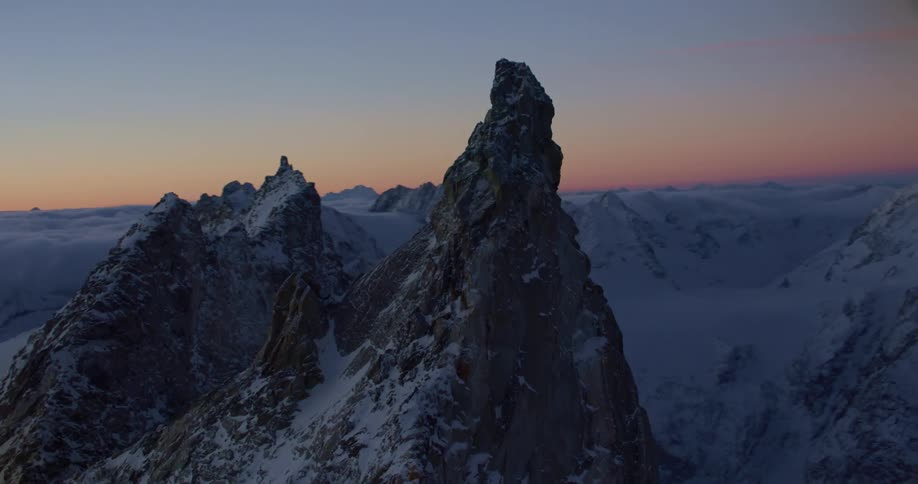 Aerial view of snowy steep mountain peak at sunset