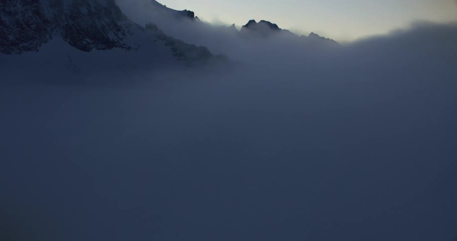 Thick clouds floating around a snowy mountain range at sunrise