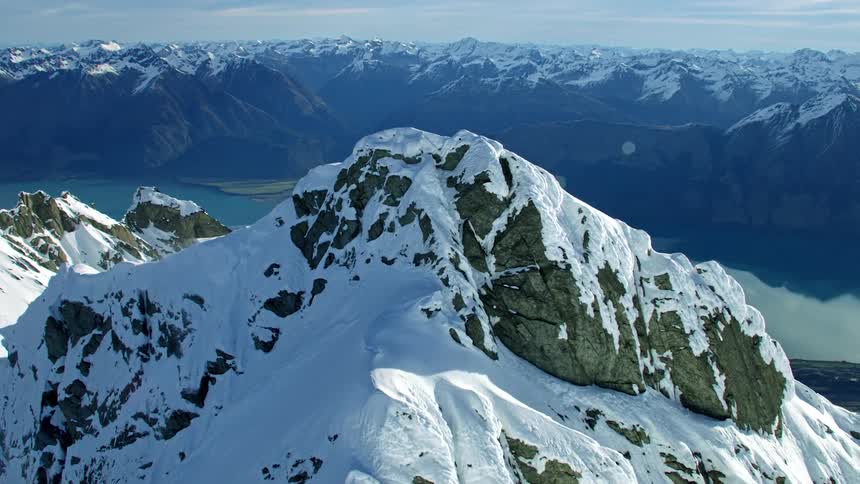 An aerial tracking of a snowy mountain range reveal blue alpine lake