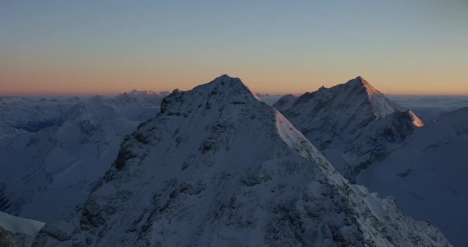 Aerial view of high snowy mountain and mountain range at sunset