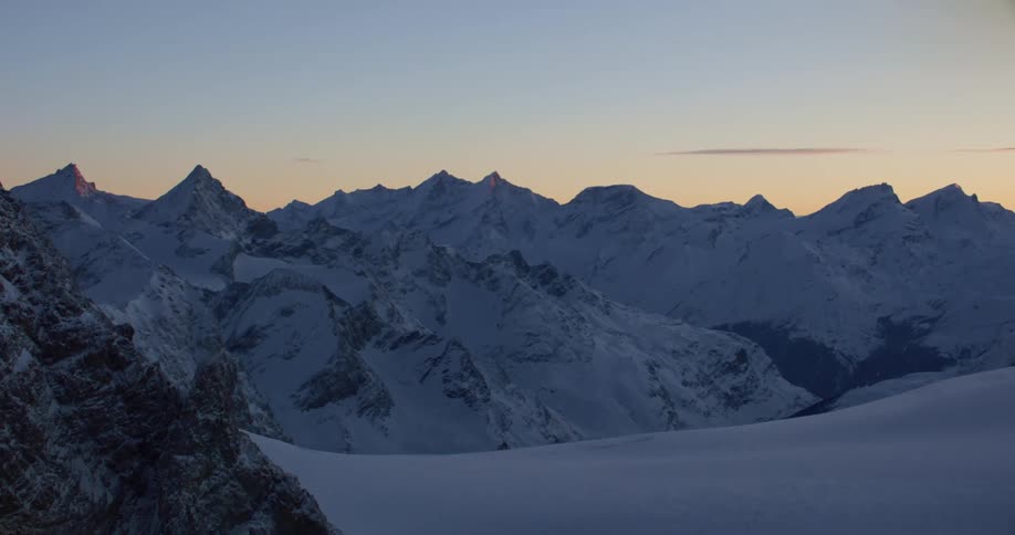 An aerial view of a snowy mountain range in the wilderness at sunrise
