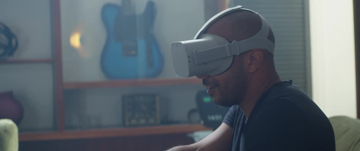 Man wearing vr goggle gestures while gaming with guitar in the background