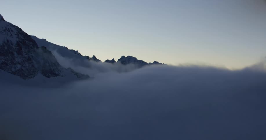 Aerial view of a thick layer of white clouds covering the slopes of a mountain range at morning