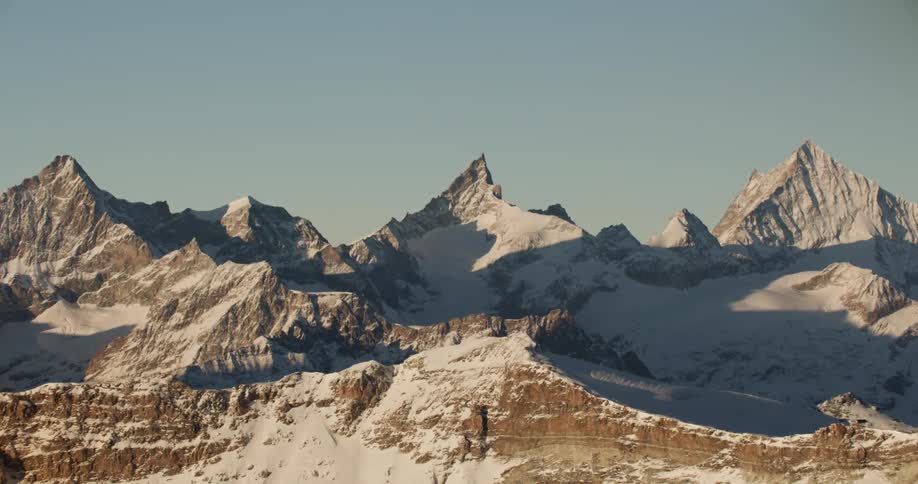 Large portions of valleys between sharp snow covered mountains remain in shadow