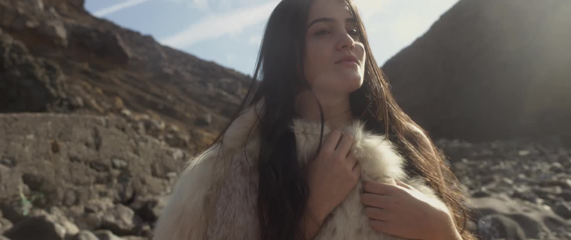 A woman wearing fur is standing outside on a windy day