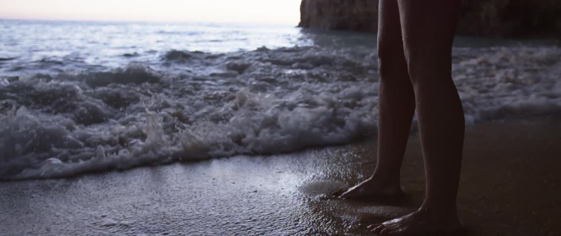 A woman wades into the ocean and bends to catch water in her hands