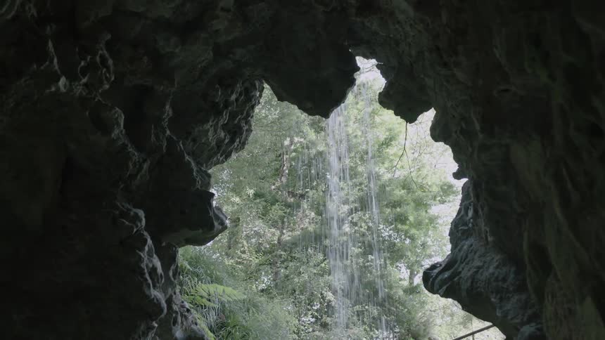 Water falls over the opening of a cave during daylight