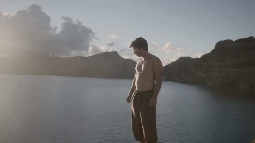 Shirtless man standing next to the water's edge