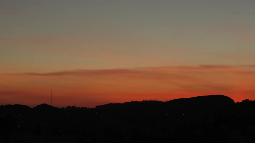 Silhouettes of hills contrast with bright red sky as scattered town lights shine dimly