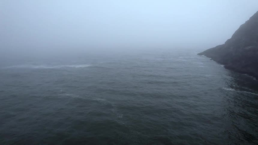 Fog shrouds the ocean off the coast of landmass during the day