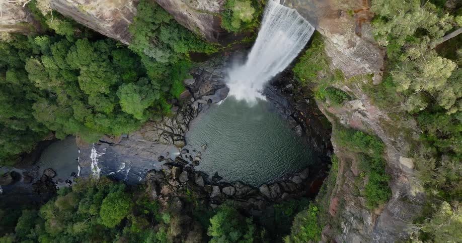 Aerial top down view of a waterfall streaming down a mountain side into a small pond
