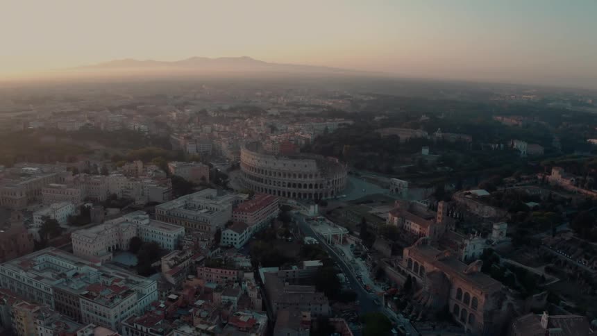 Sun shines brightly on horizon near foggy mountain as bus moves along street past colosseum