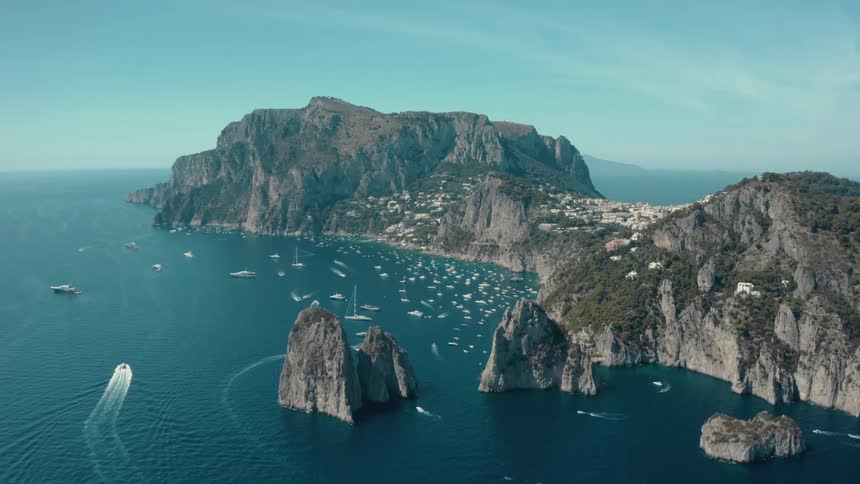 Boats sail toward a town nestled on a peninsula below tall cliffs