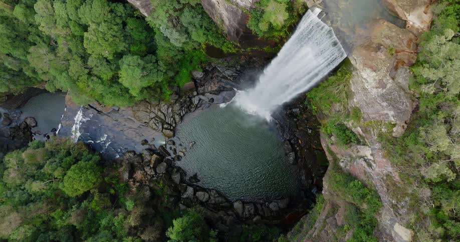 Top down aerial view of a river and waterfall flowing through a forest in the mountain