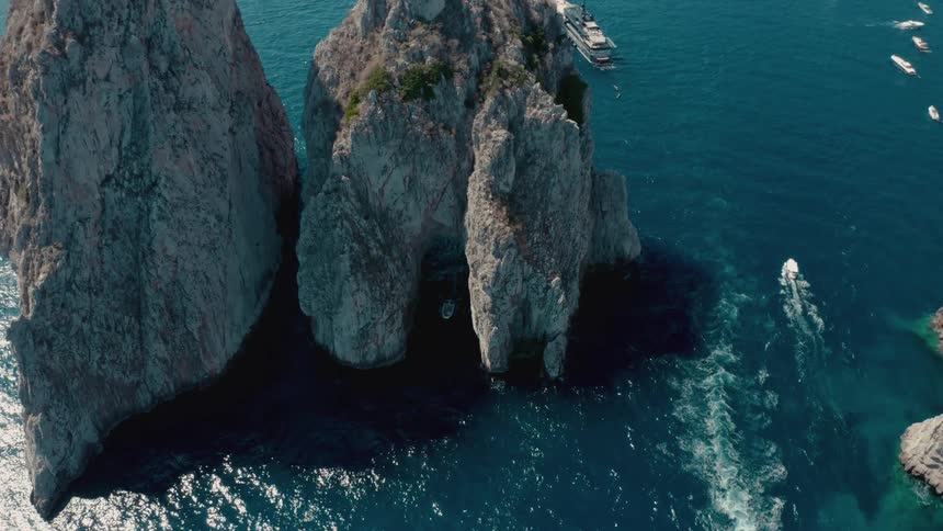 Aerial view of boats sailing through the openings of big rock promontories on the coast