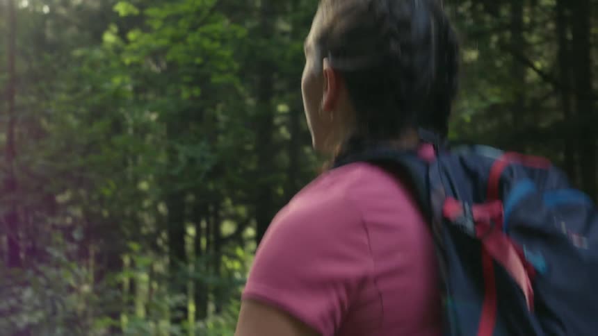 A teenage girl with braids hiking in a forest with a backpack
