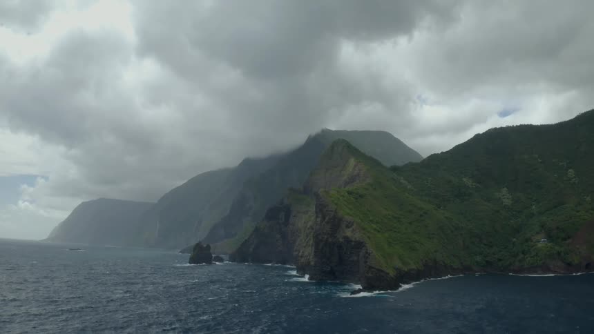 The mountainous coastline of a landmass under a cloudy daytime sky